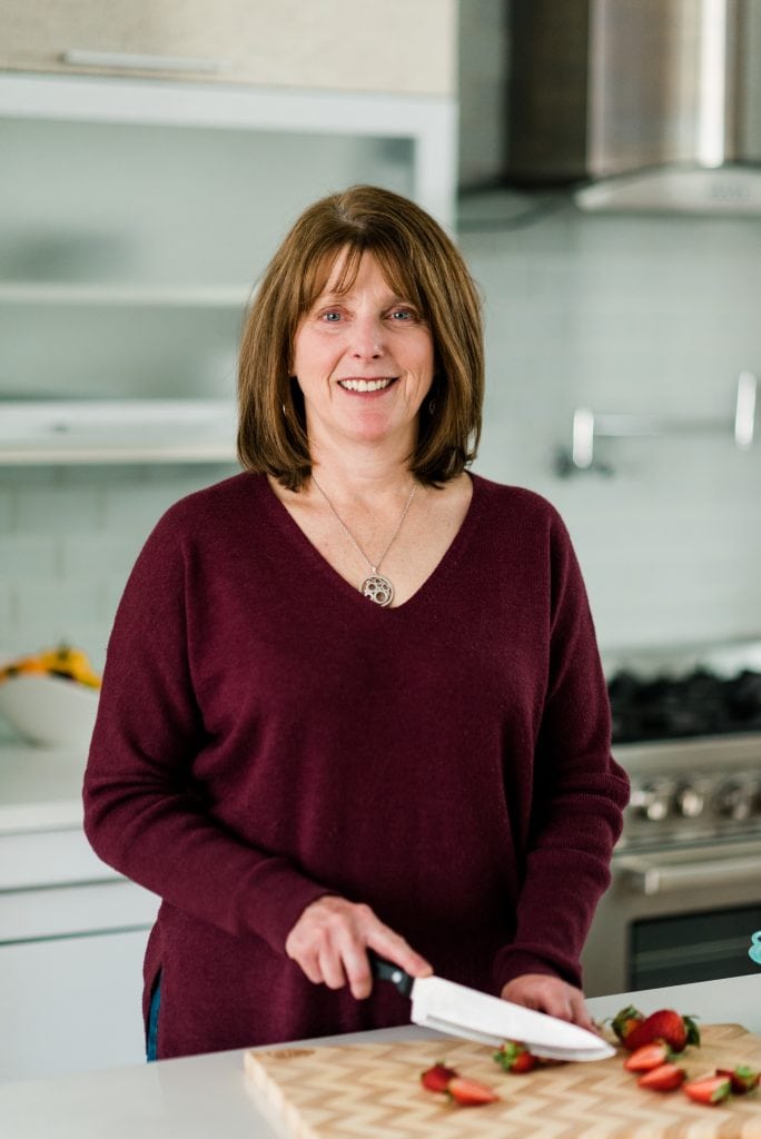 Beth Crowded Kitchen headshot - slicing strawberries on wood cutting board