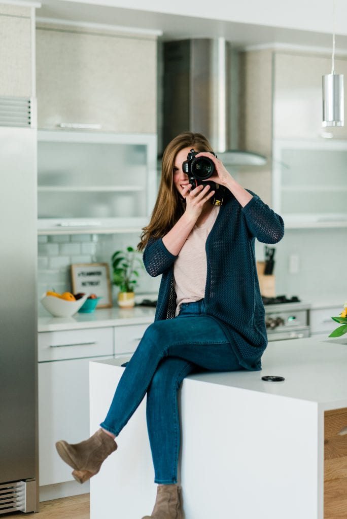 Crowded Kitchen headshot - Lexi holding camera and sitting on counter