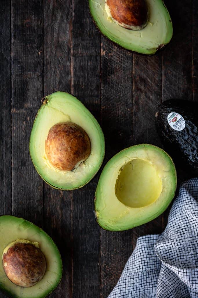 Overhead view of multiple avocados cut in half on a wood background