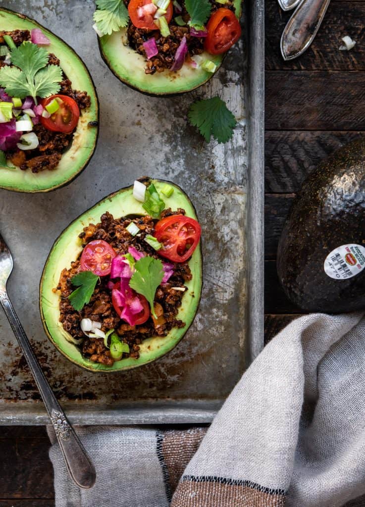 Overhead close up view of vegan taco stuffed avocados on a sheet pan on wood background