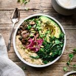 Overhead view of savory vegan oatmeal with mushrooms, kale, avocado and pickled onion in a white bowl on wood background