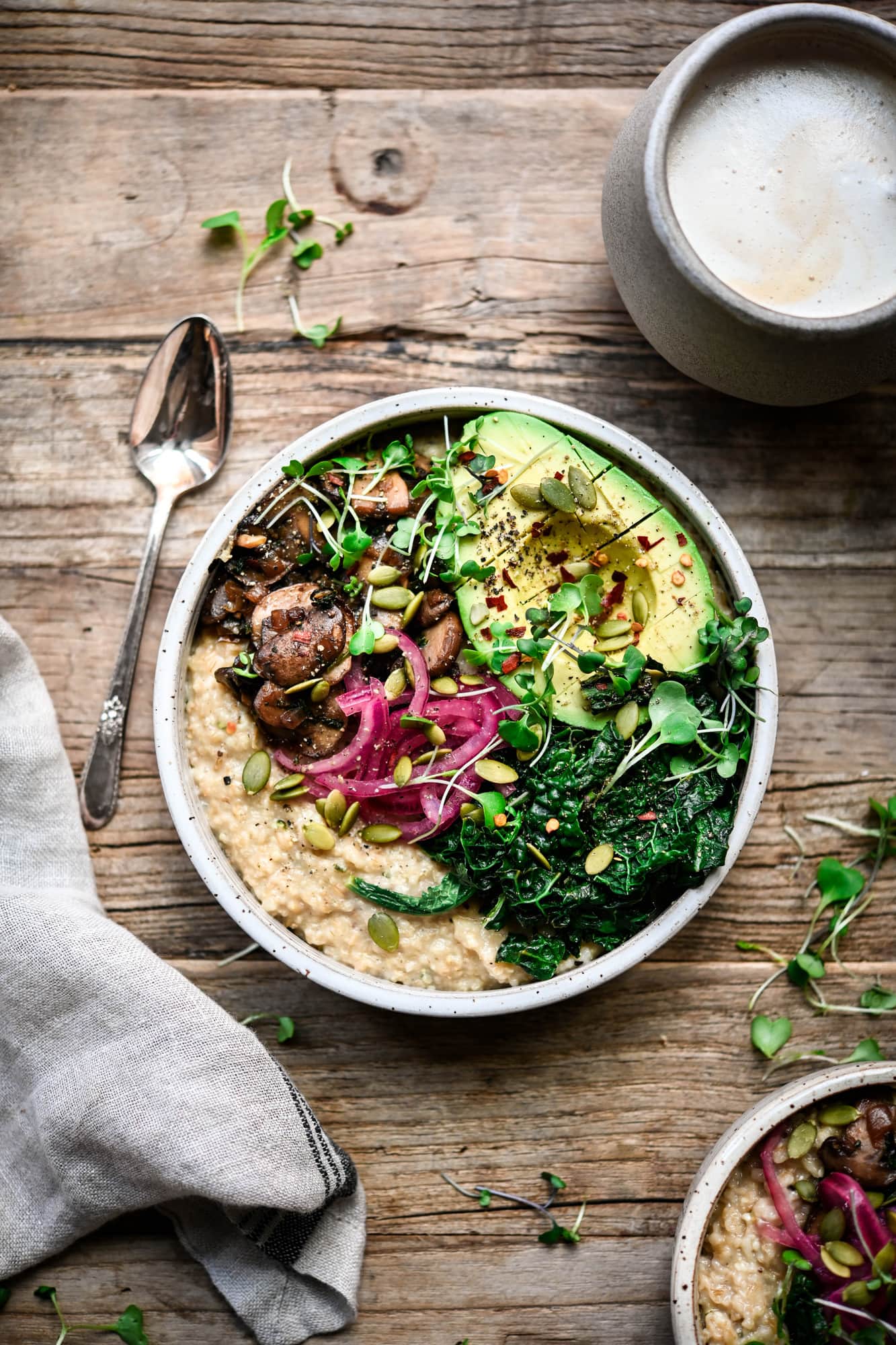 Overhead view of savory vegan oatmeal with mushrooms, kale, avocado and pickled onion in a white bowl on wood background