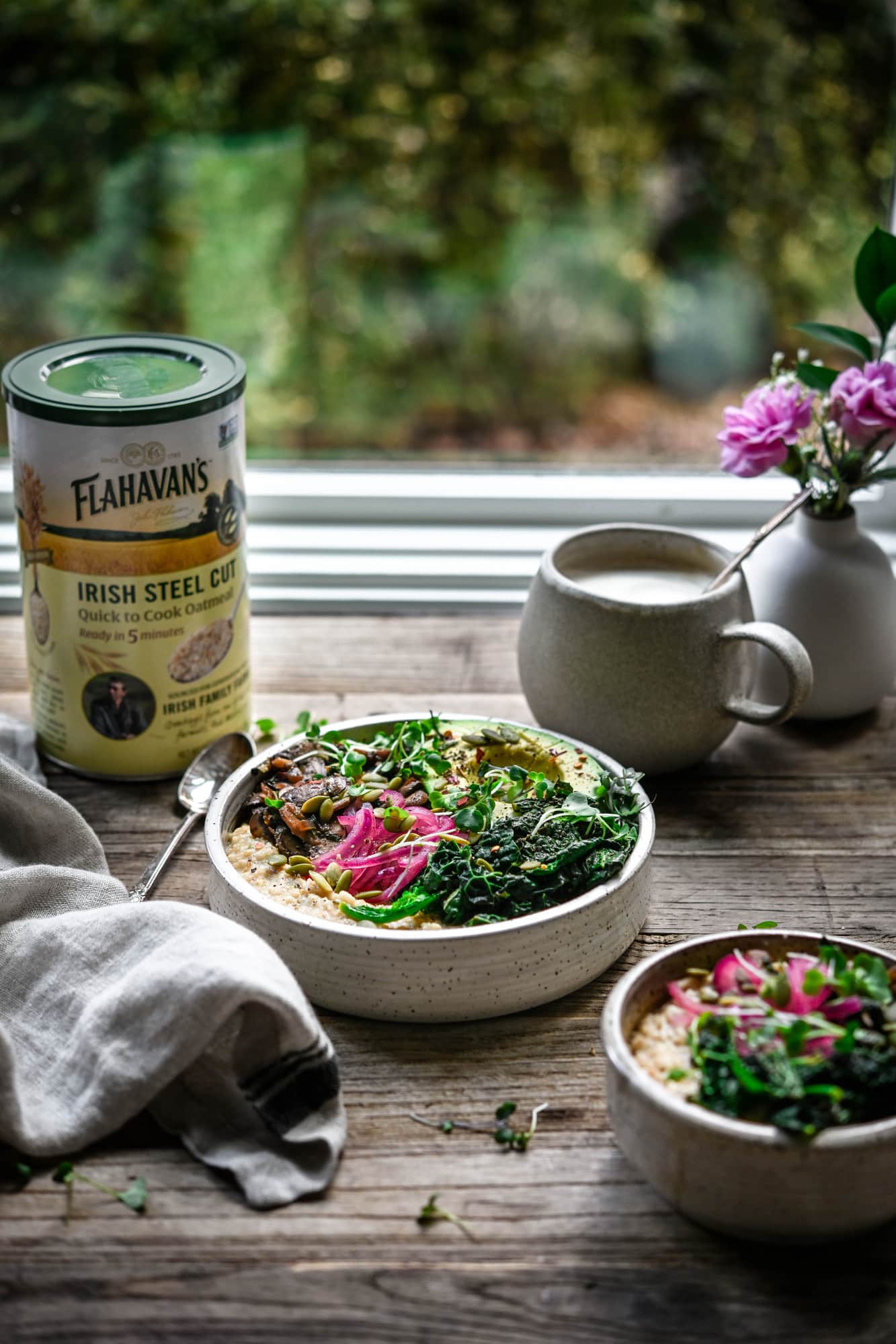 Side view of bowl of vegan savory oatmeal on a wood table with window and greenery in background