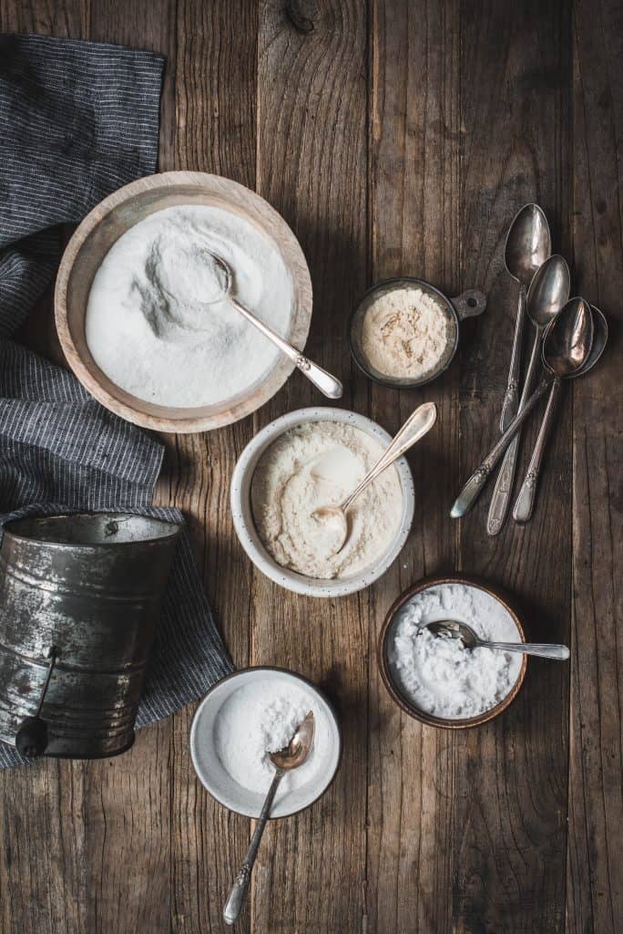 Overhead of ingredients for gluten free flour blend in different sized bowls with spoons on a wood table
