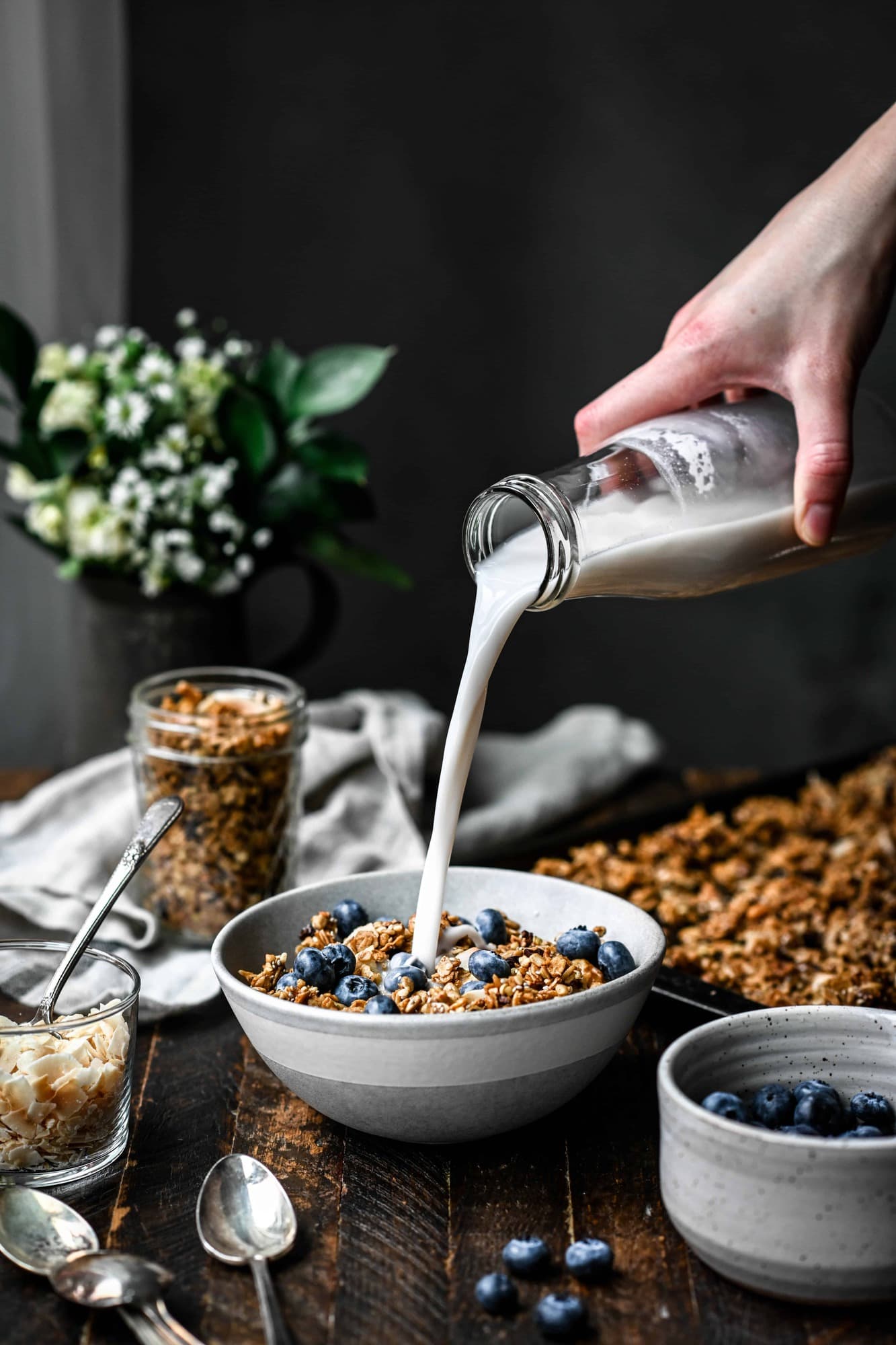 Pouring milk into a bowl of granola and blueberries on a wood table