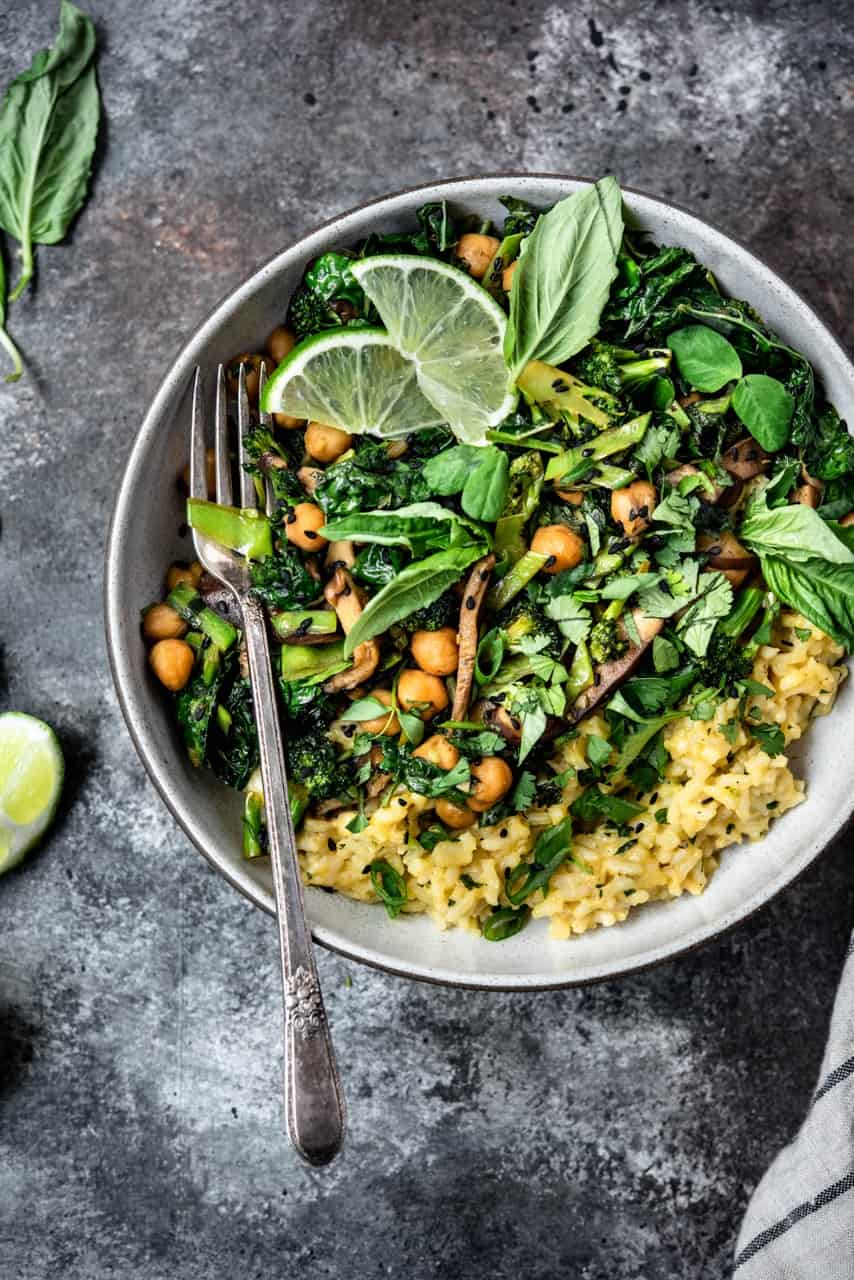 Overhead view of green curry coconut rice with stir fried vegetables, mushrooms, chickpeas and herbs with a striped linen