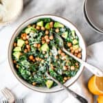 Overhead of kale tahini caesar salad with crunchy chickpeas in a white bowl on marble surface
