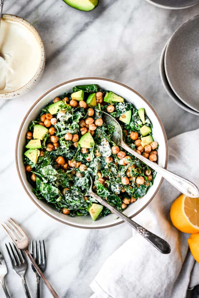 Overhead of kale tahini caesar salad with crunchy chickpeas in a white bowl on marble surface