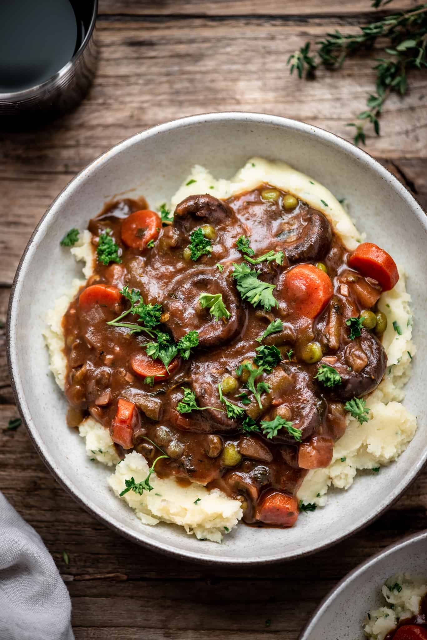 Overhead view of vegan mushroom stew served over mashed potatoes in a white bowl on a wood table