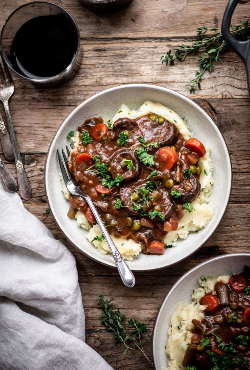 Overhead view of vegan mushroom stew served over mashed potatoes in a white bowl on a wood table