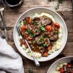 Overhead view of vegan mushroom stew served over mashed potatoes in a white bowl on a wood table