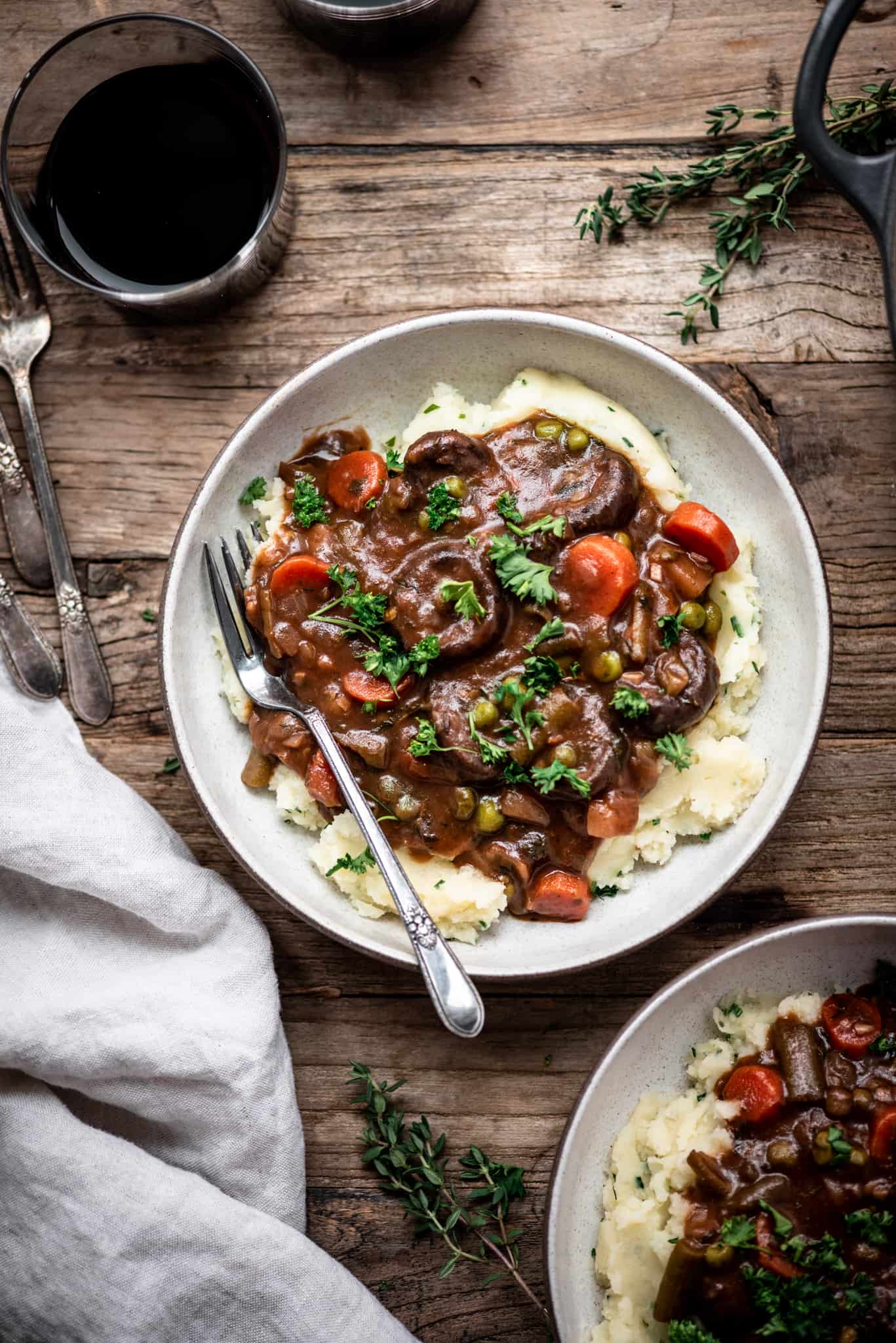 Overhead view of vegan mushroom stew served over mashed potatoes in a white bowl on a wood table