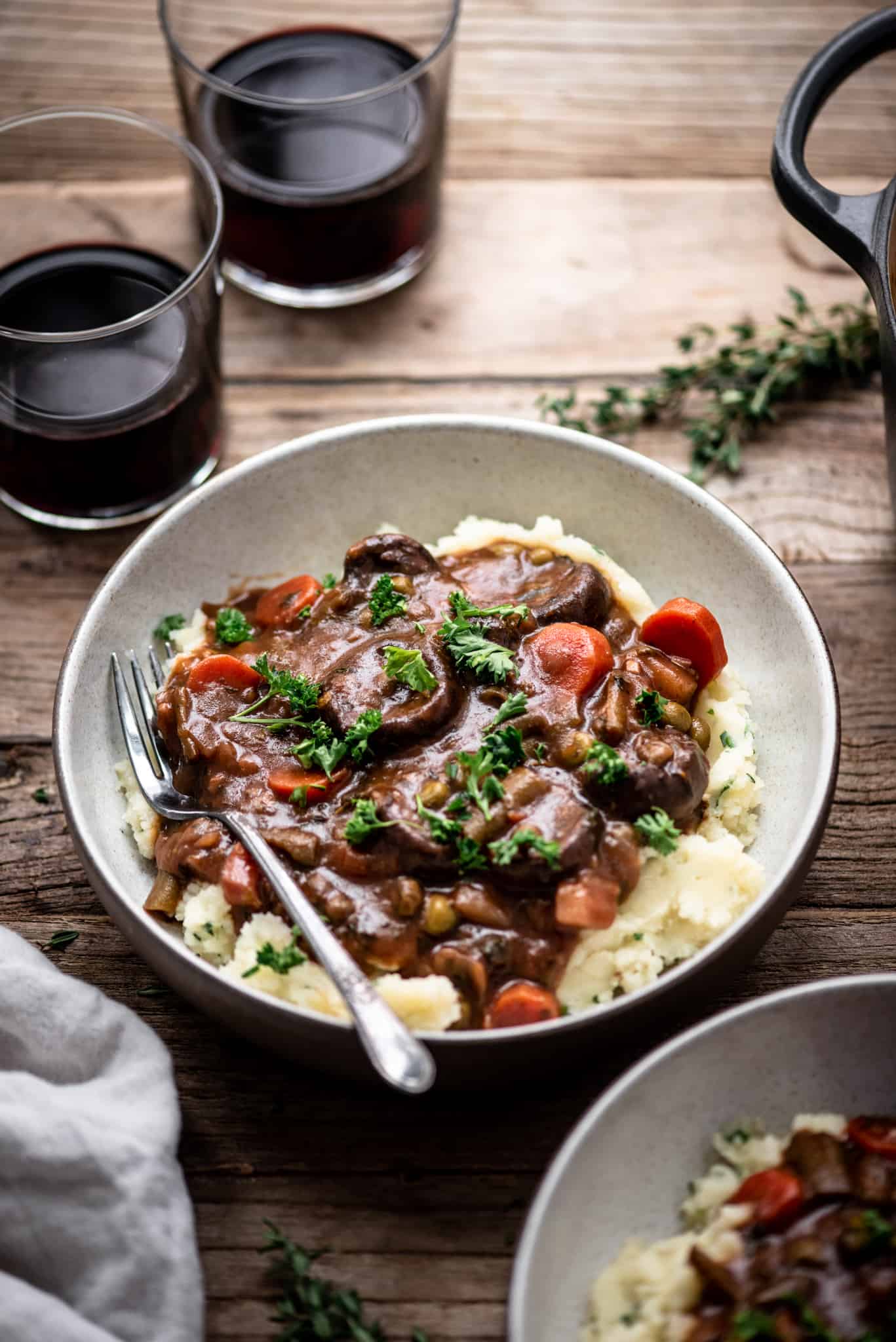 Side view of vegan mushroom stew served over mashed potatoes in a white bowl on a wood table