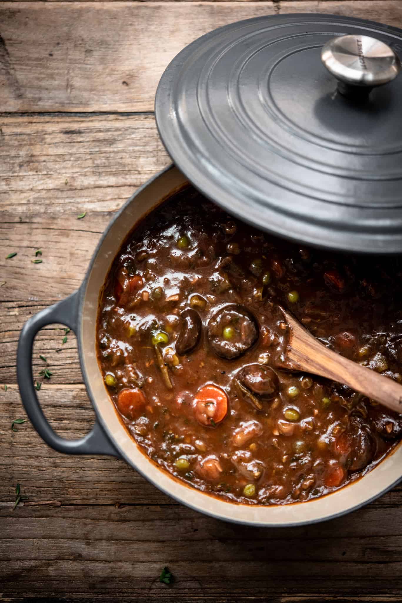 Overhead view of vegan mushroom stew in a large gray pot on a wood table