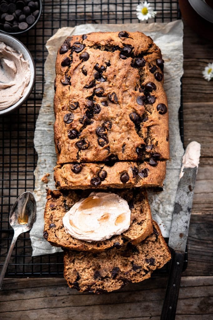 Overhead view of gluten free banana bread with maple cream cheese spread on a cooling rack and parchment paper