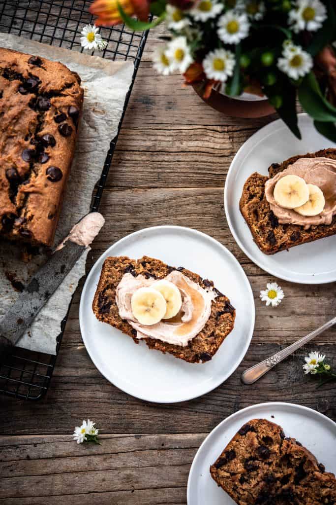 Overhead view of slice of gluten free banana bread on white plate with cinnamon cream cheese and banana slices