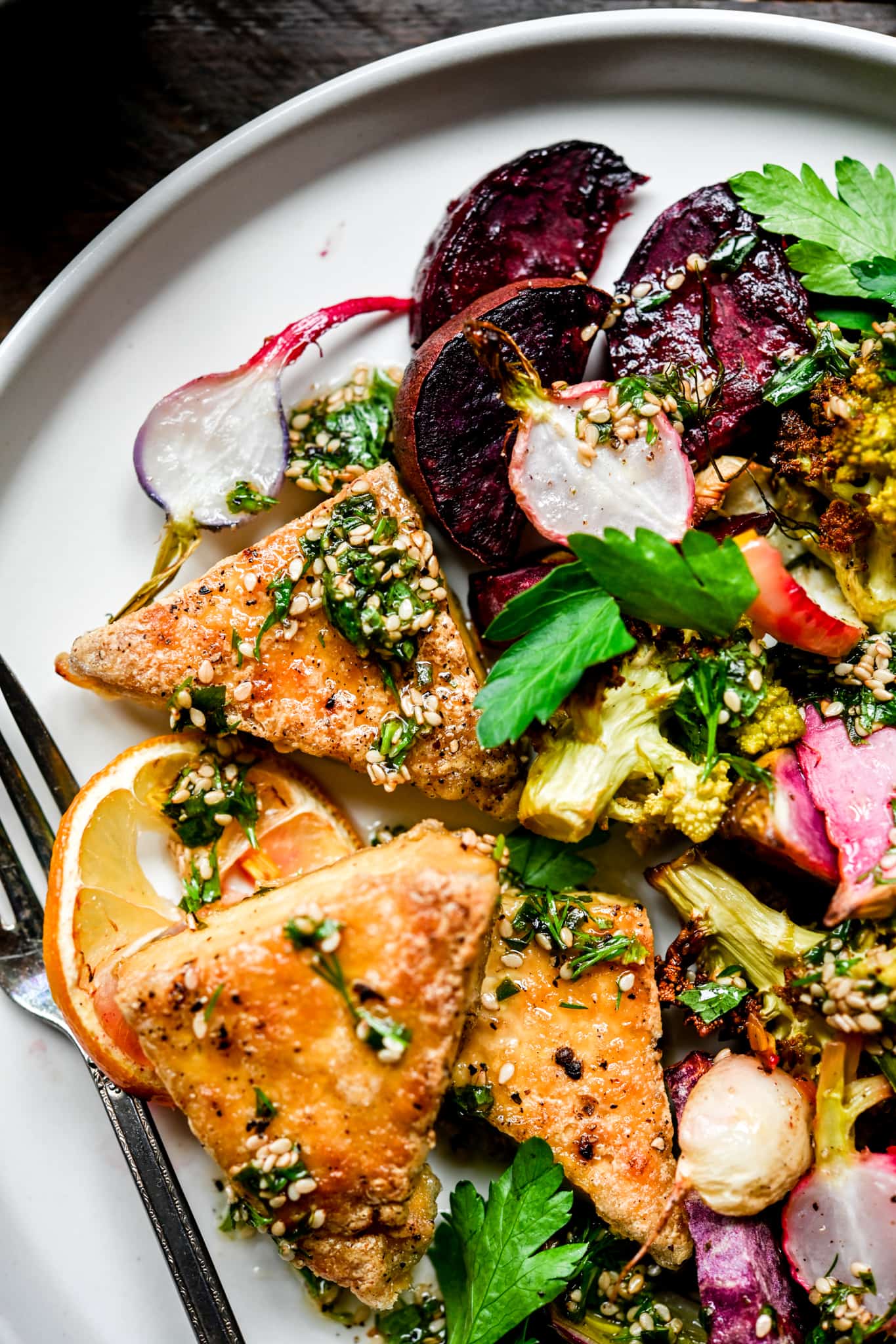 Overhead of roasted vegetables and tofu on a white plate with herb sauce