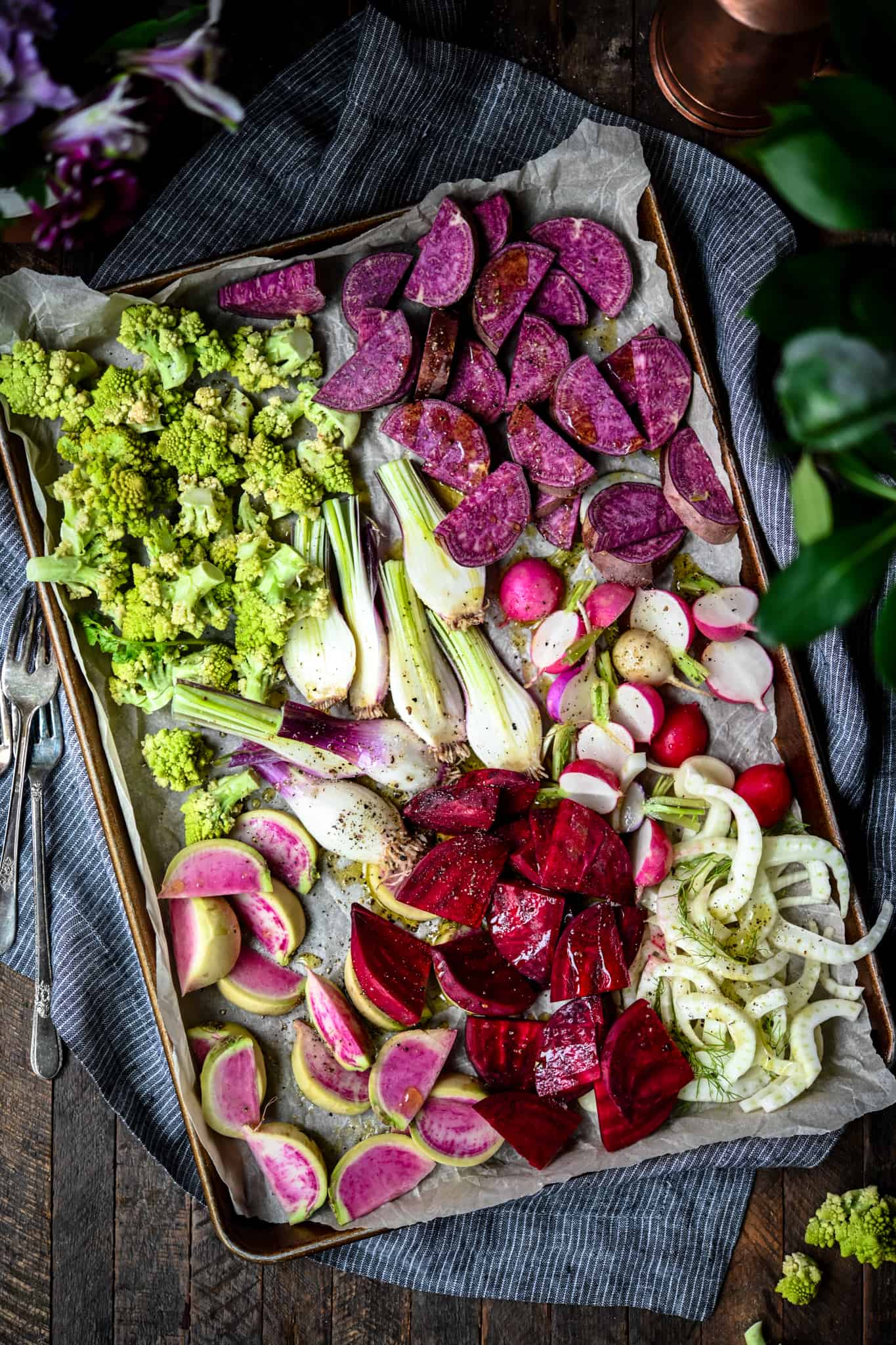 Overhead of sheet pan with uncooked purple, pink and green vegetables
