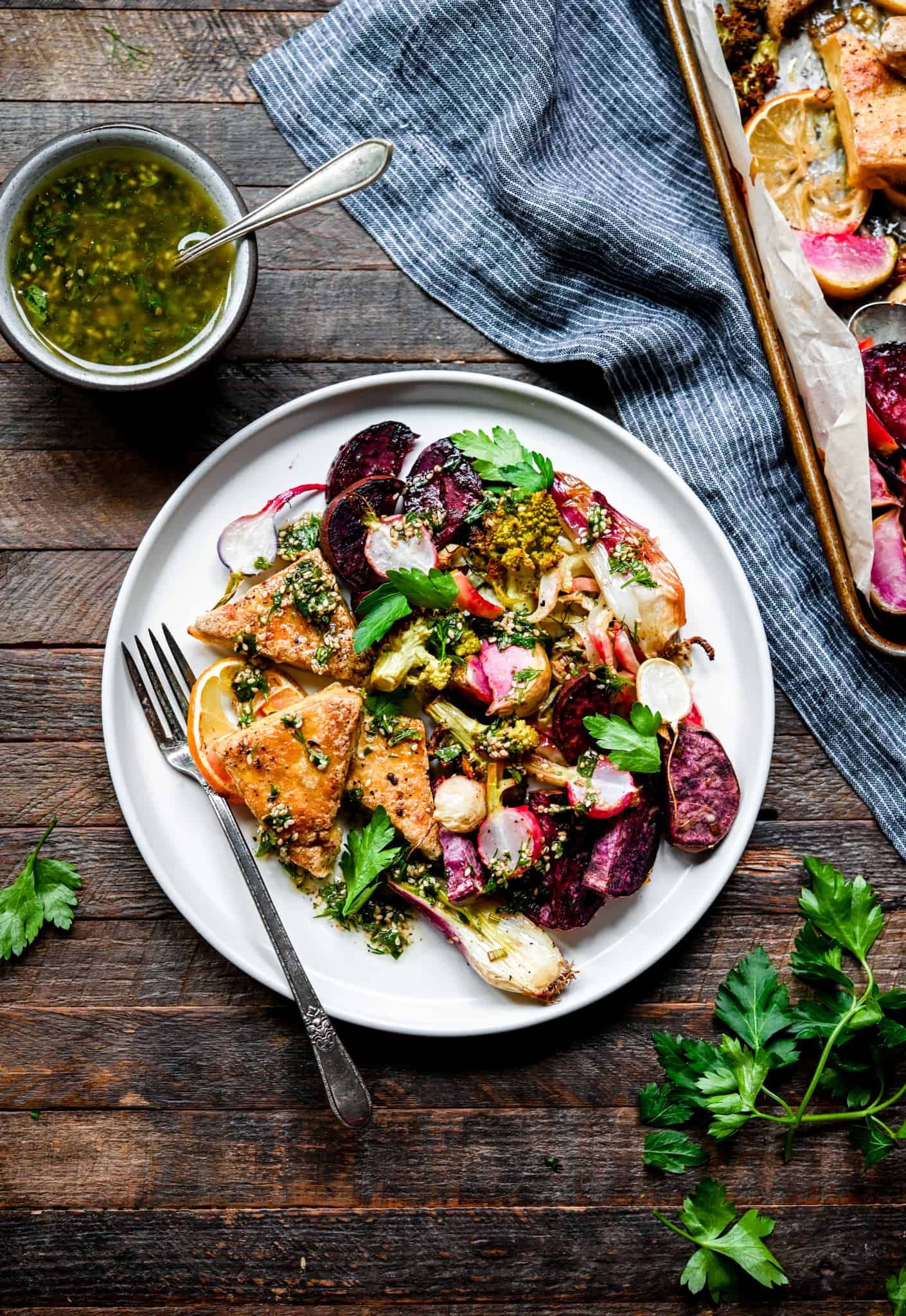 Overhead of roasted vegetables and tofu on a white plate with herb sauce