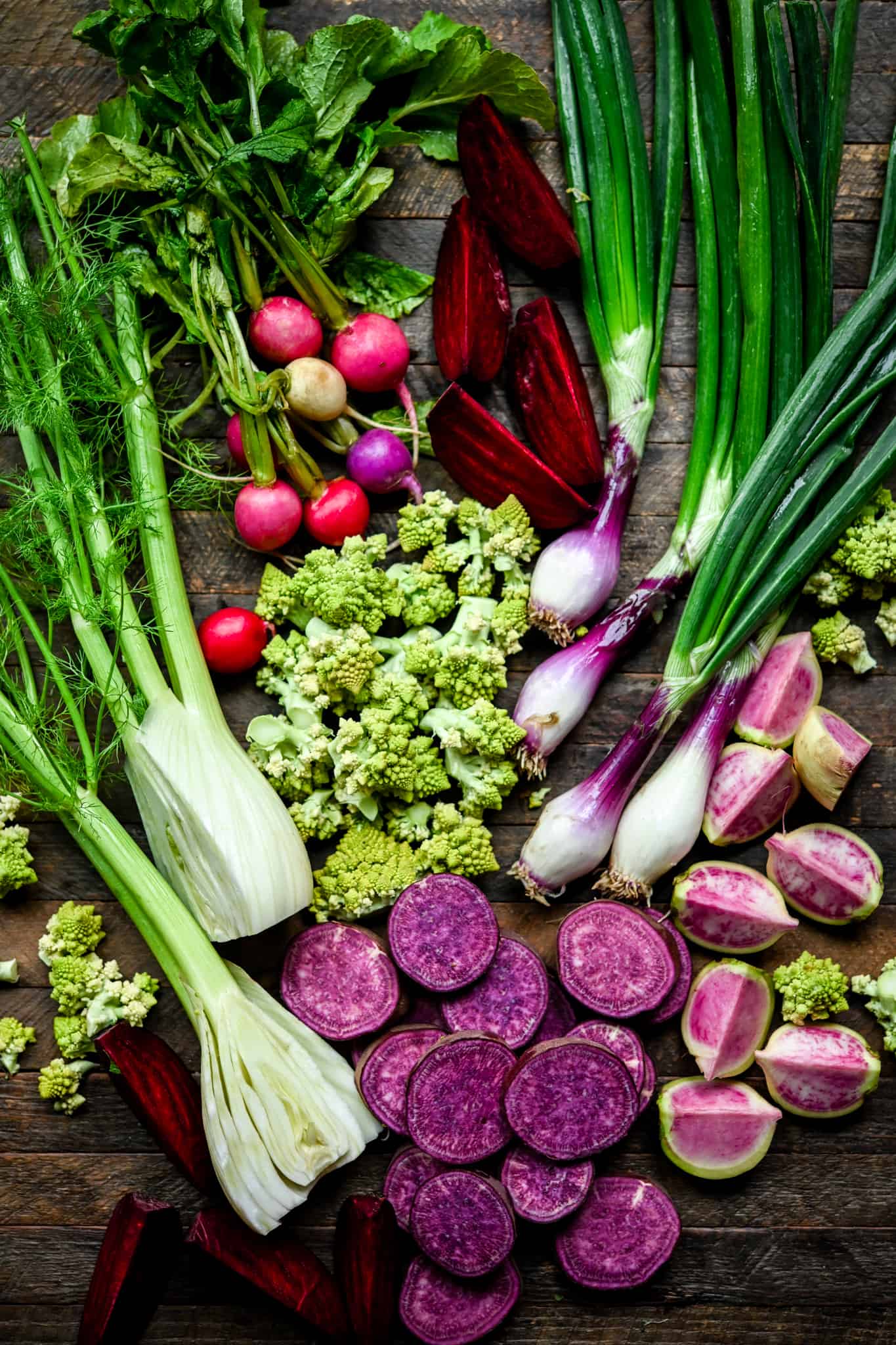 Overhead view of raw purple, green, pink and red vegetables on wood background