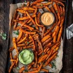 Overhead of spiced sweet potato fries on an antique baking sheet with fresh herbs and aioli