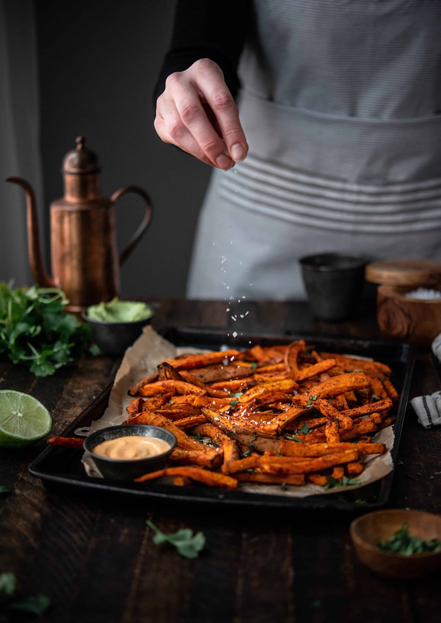 Person sprinkling flaky salt onto homemade sweet potato fries on a baking sheet