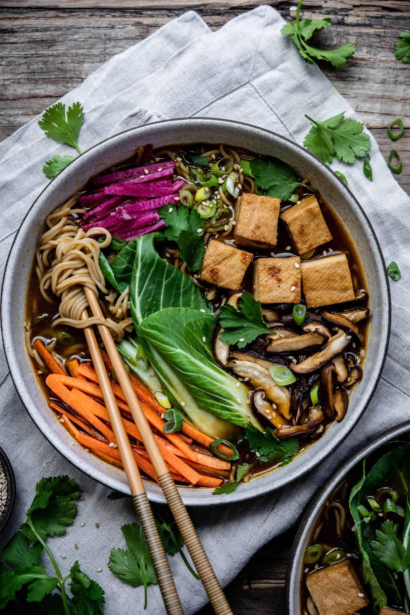 Close up of homemade vegan ramen in a white bowl with chopsticks, bok choy, tofu, mushrooms, carrots and noodles