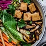 Close up of homemade vegan ramen in a white bowl with chopsticks, bok choy, tofu, mushrooms, carrots and noodles