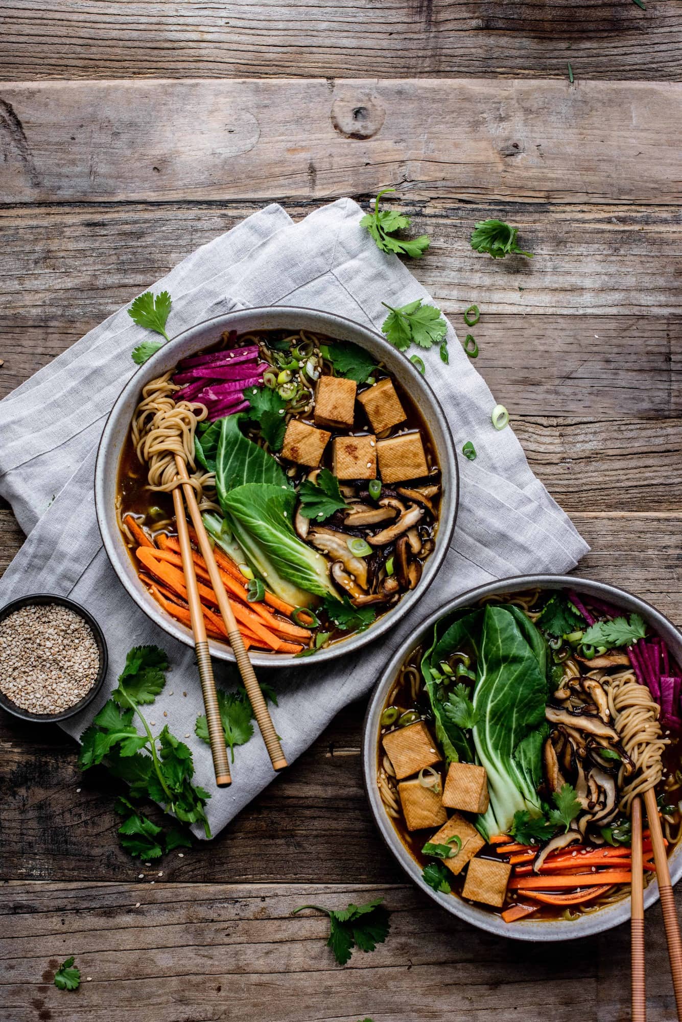 Overhead view of homemade vegan ramen in a white bowl with chopsticks, bok choy, tofu, mushrooms, carrots and noodles