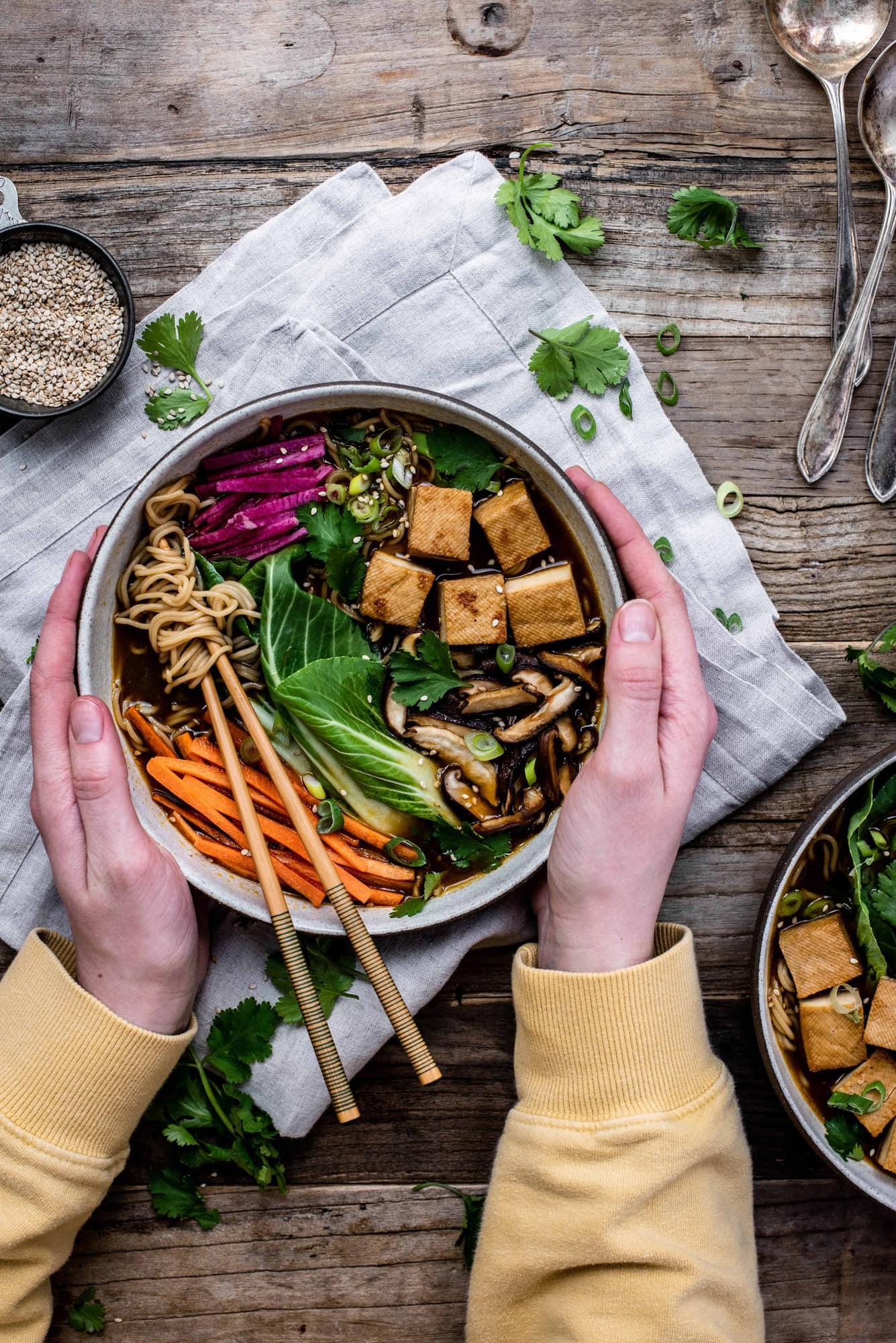 Overhead view of homemade vegan ramen in a white bowl with chopsticks, bok choy, tofu, mushrooms, carrots and noodles