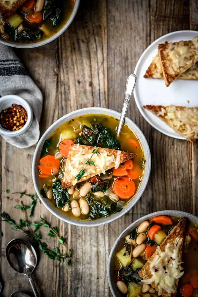 Overhead view of white bean kale soup in a grey bowl on a wood table