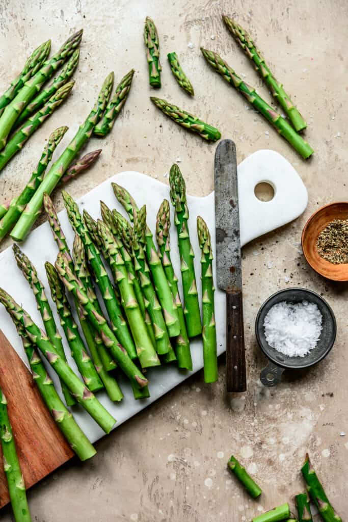 Overhead view of beautiful food photography of asparagus spears on a white marble cutting board on a light tan background