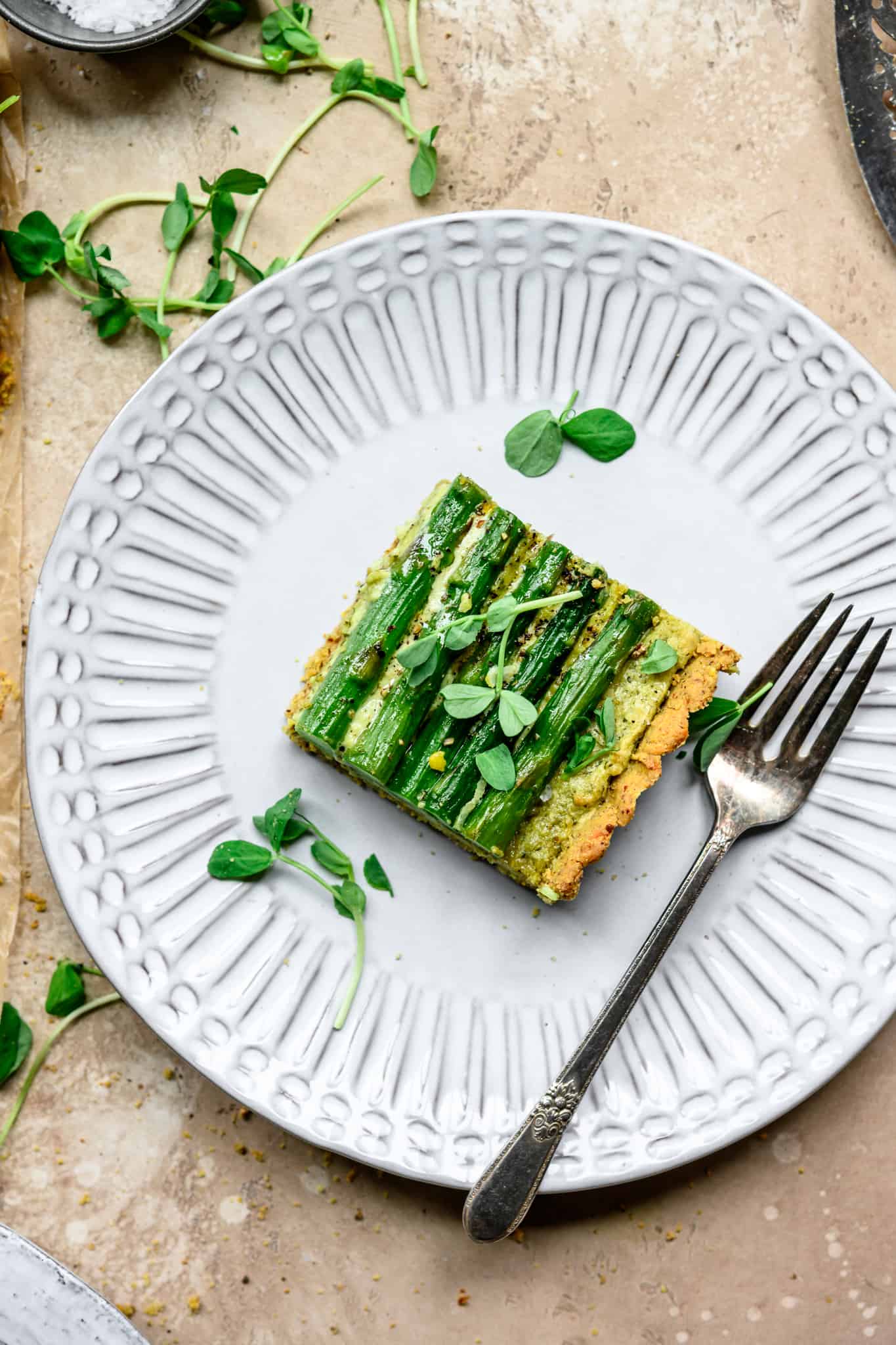 Overhead view of slice of vegan ricotta and asparagus tart on a white plate with fork