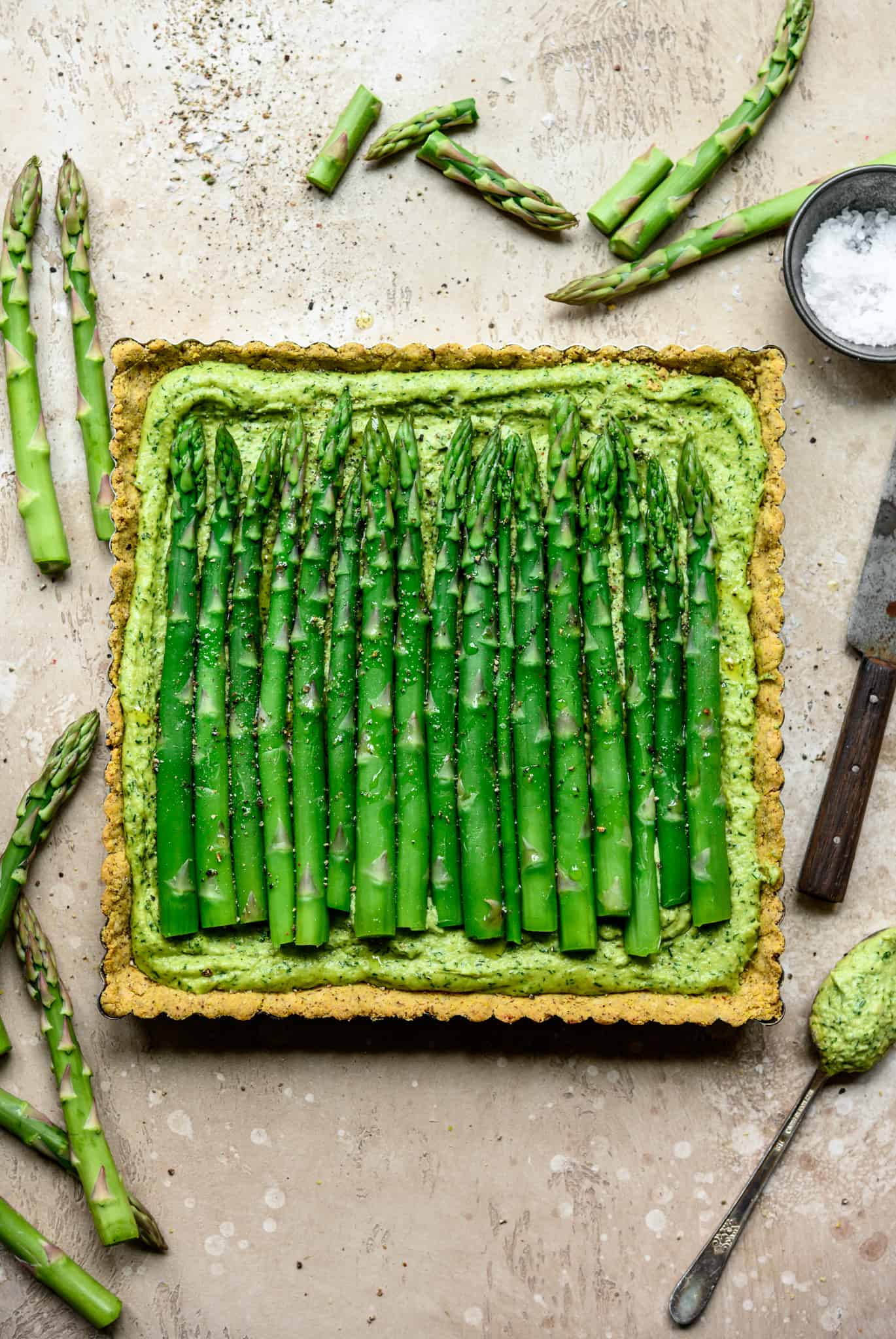 Overhead view of vegan ricotta and asparagus tart with a cornmeal crust on light tan background