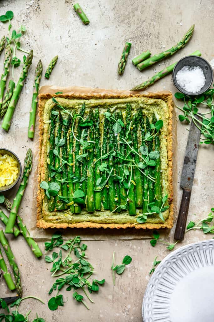 Savory asparagus tart with fresh greens, homemade crust, and vibrant green toppings. Perfect for spring and brunch.