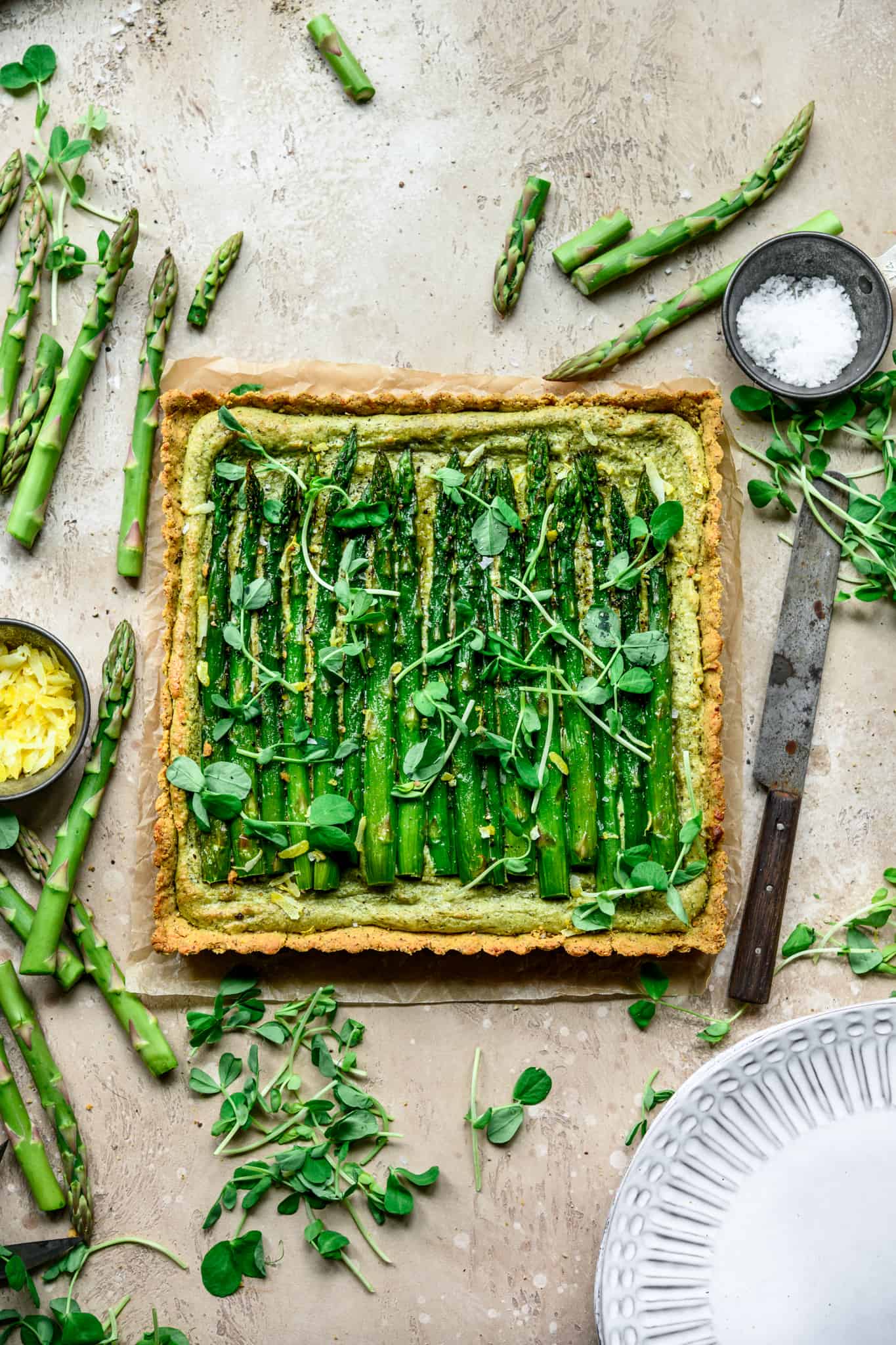 Overhead view of vegan ricotta and asparagus tart with a cornmeal crust on light tan background
