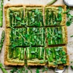 Overhead view of vegan ricotta and asparagus tart with a cornmeal crust sliced into squares on light tan background