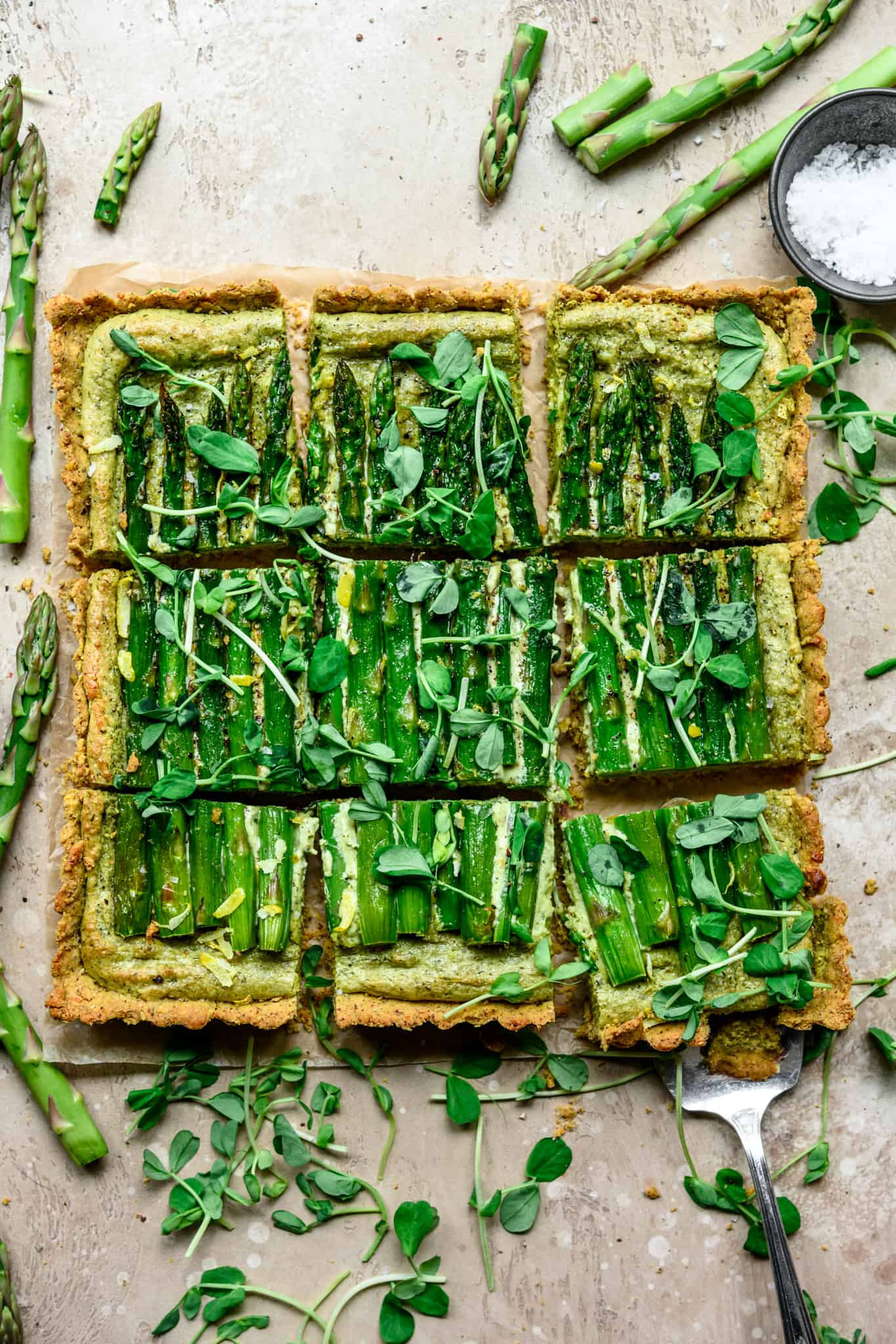 Overhead view of vegan ricotta and asparagus tart with a cornmeal crust sliced into squares on light tan background