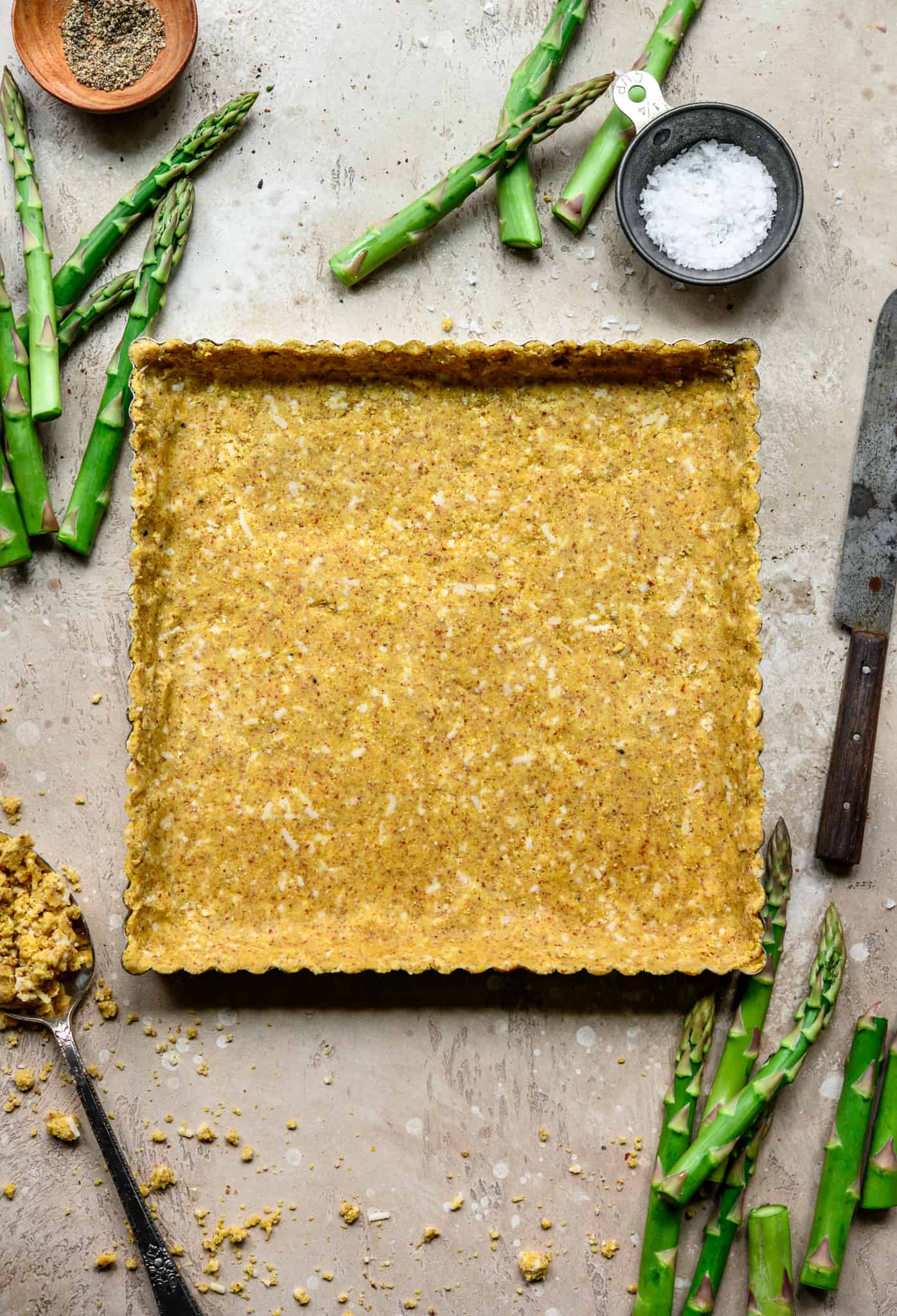 Overhead view of cornmeal crust pressed into square tart pan on light tan background