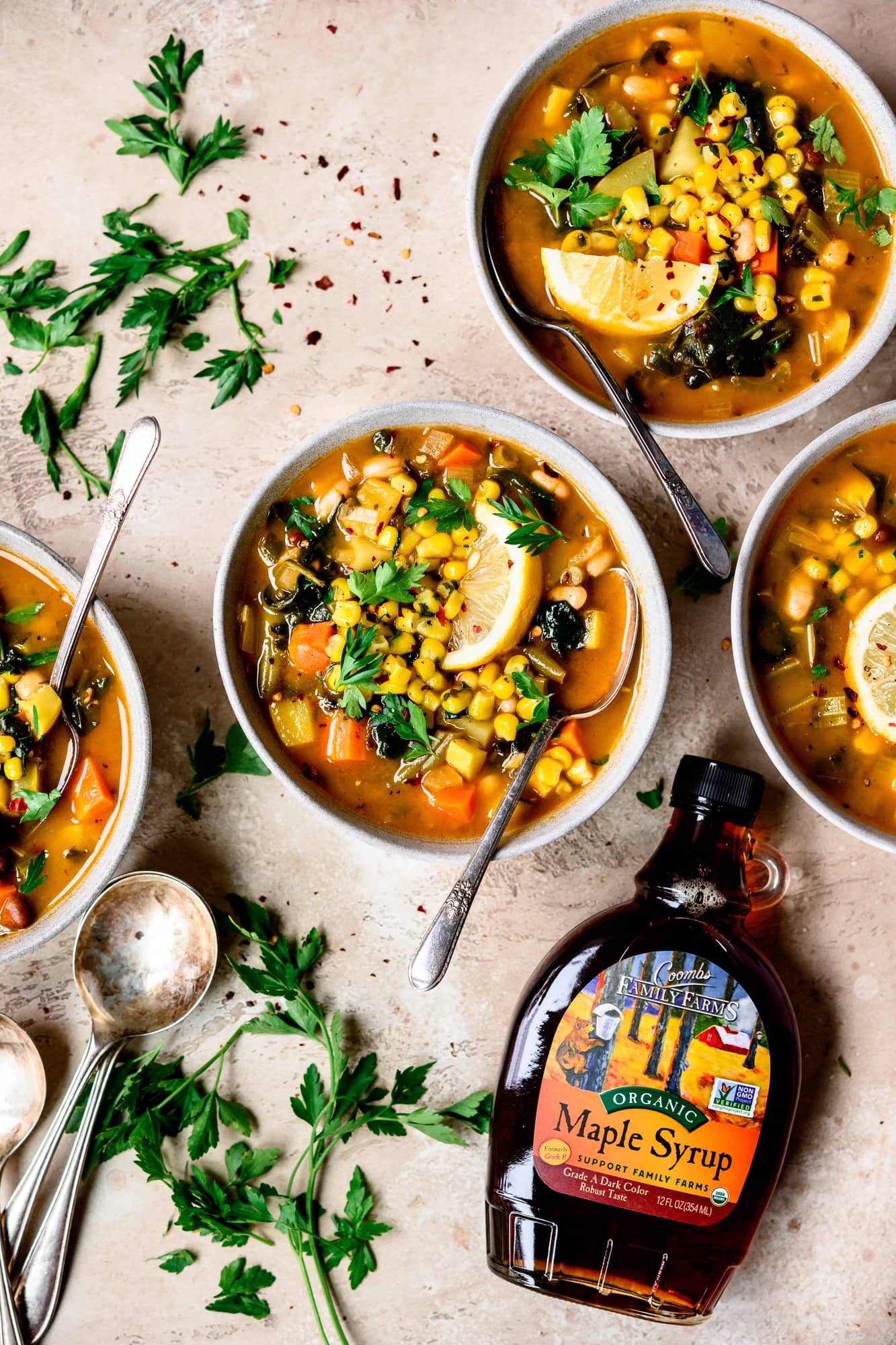 Overhead view of white bean vegetable soup with maple in light grey bowls with spoons and lemon garnish