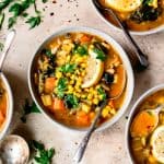Overhead view of white bean vegetable soup with maple in light grey bowls with spoons and lemon garnish