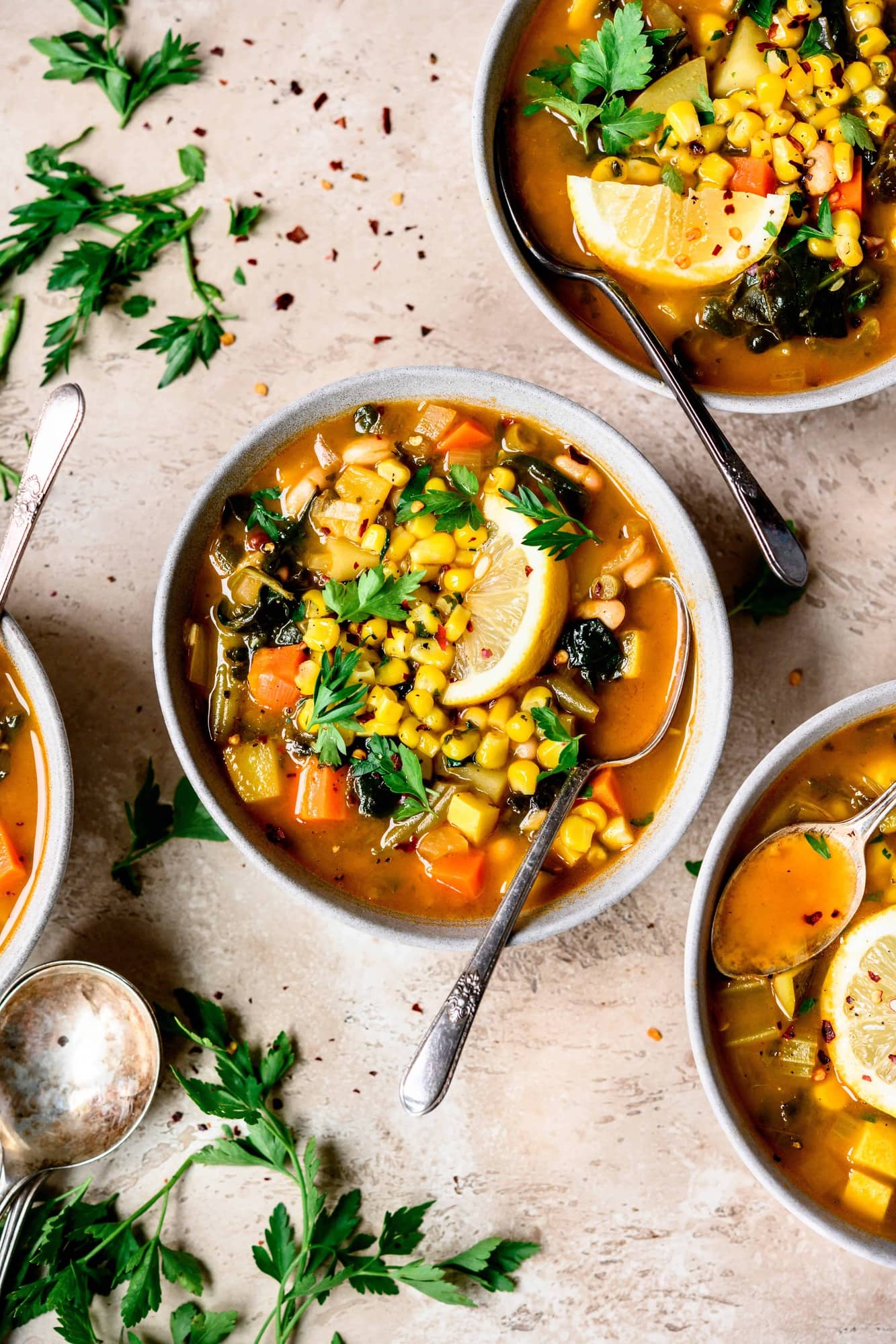 Overhead view of white bean vegetable soup with maple in light grey bowls with spoons and lemon garnish