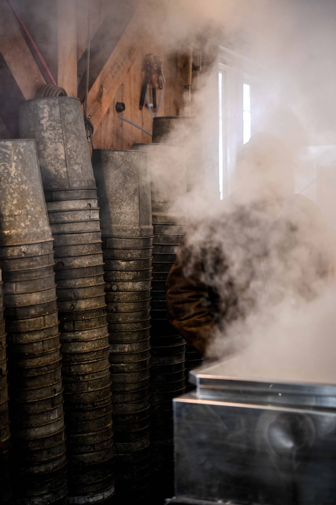 View of maple sap collection buckets in Sugarhouse with steam in foreground