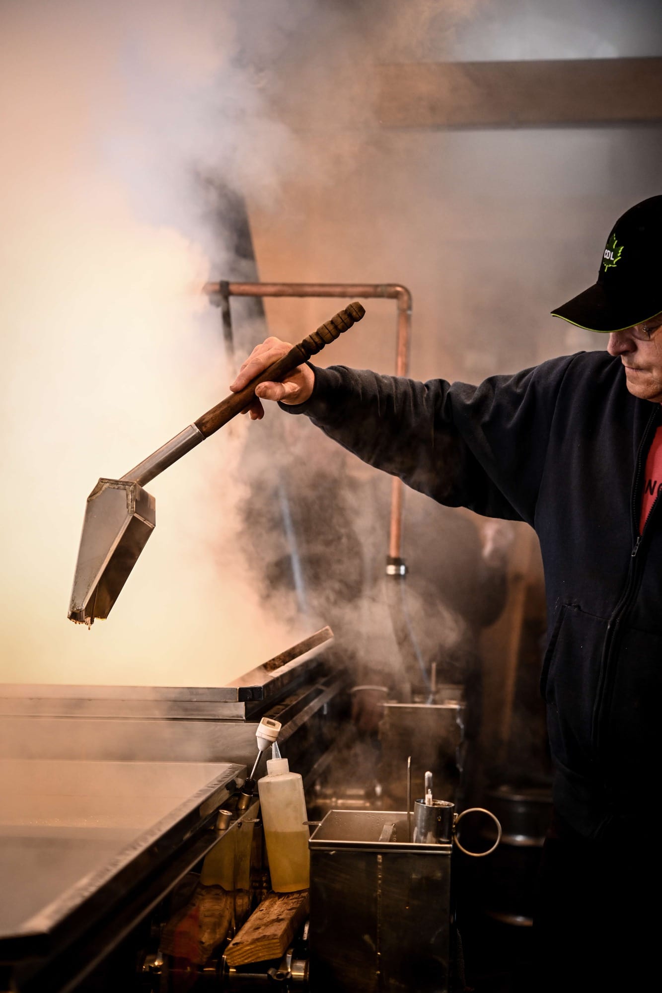 Man in maple sugarhouse testing viscosity of maple syrup