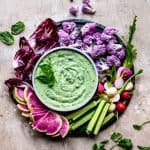 Overhead of herby whipped tofu dip with fresh colorful vegetables on a round platter