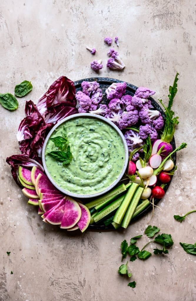 Overhead of herby whipped tofu dip with fresh colorful vegetables on a round platter