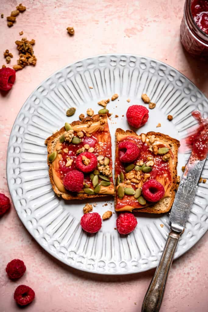 Overhead view of peanut butter and rhubarb compote toast on a white plate with fresh raspberries