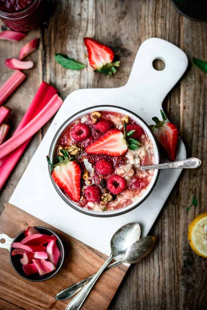 Overhead view of oatmeal with rhubarb compote and fresh berries on a marble serving board