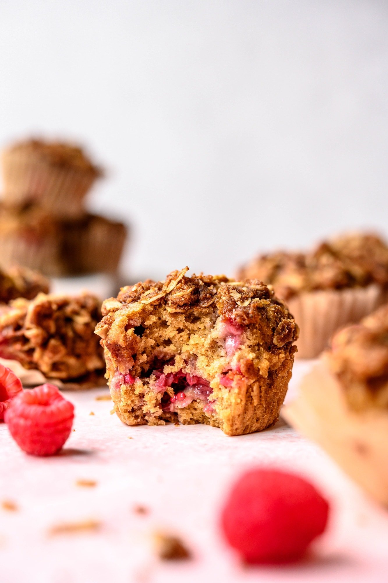 Side view of vegan raspberry rhubarb muffins with bite taken out on pink background