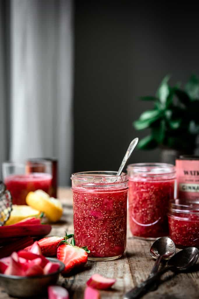 Side view of jar of rhubarb vanilla chia compote on a wood table, dark and moody photo